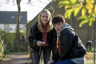 Twee tieners, een jongen en een meisje, zitten buiten in een park en kijken naar een telefoon.